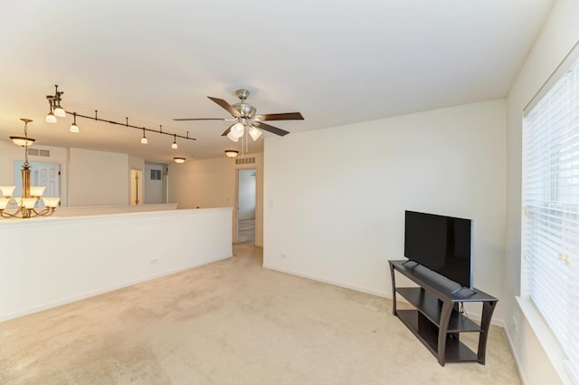 living room with ceiling fan with notable chandelier, track lighting, and light colored carpet