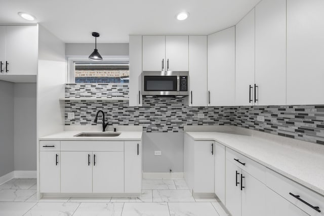 kitchen featuring sink, backsplash, white cabinets, and hanging light fixtures