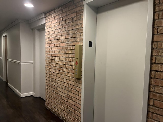 hall with elevator, dark hardwood / wood-style flooring, and brick wall