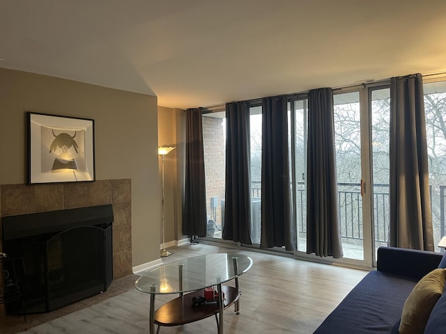 living room with a wall of windows, plenty of natural light, a tiled fireplace, and light hardwood / wood-style flooring