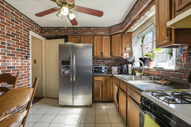 kitchen featuring brick wall, under cabinet range hood, brown cabinets, stainless steel fridge, and a sink