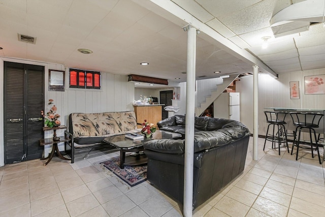 living room featuring visible vents, stairs, a paneled ceiling, wood walls, and tile patterned floors