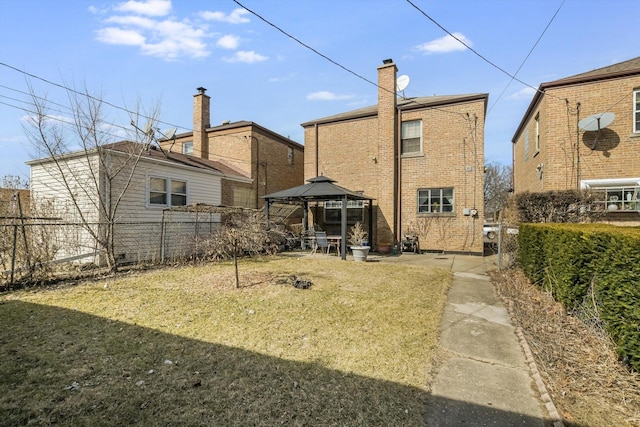 back of property with a gazebo, brick siding, a fenced backyard, and a chimney