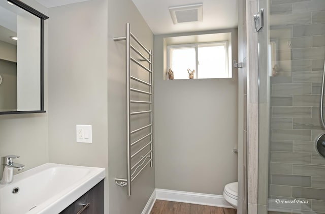 bathroom with hardwood / wood-style flooring, vanity, a tile shower, and toilet