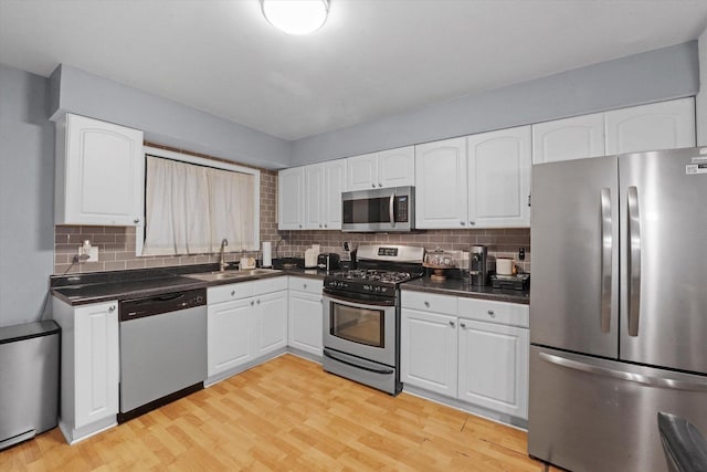 kitchen with appliances with stainless steel finishes, light hardwood / wood-style flooring, backsplash, sink, and white cabinetry