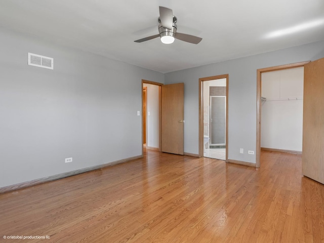 unfurnished bedroom with baseboards, visible vents, a closet, a walk in closet, and light wood-type flooring