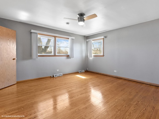 spare room with ceiling fan, visible vents, baseboards, and wood finished floors