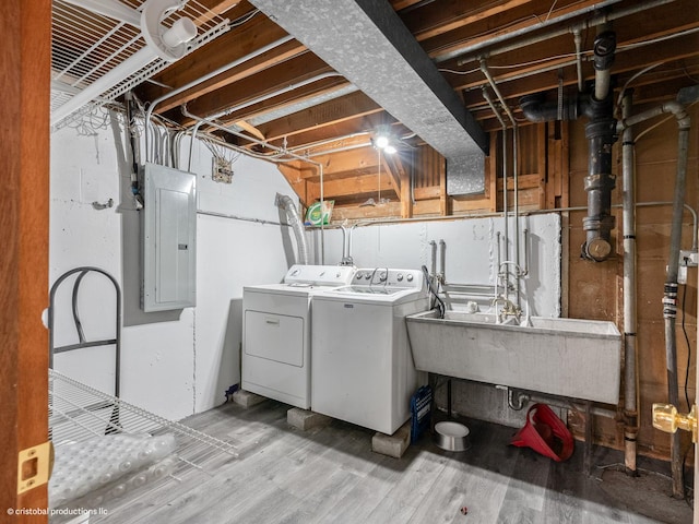 laundry area with electric panel, a sink, wood finished floors, washing machine and dryer, and laundry area