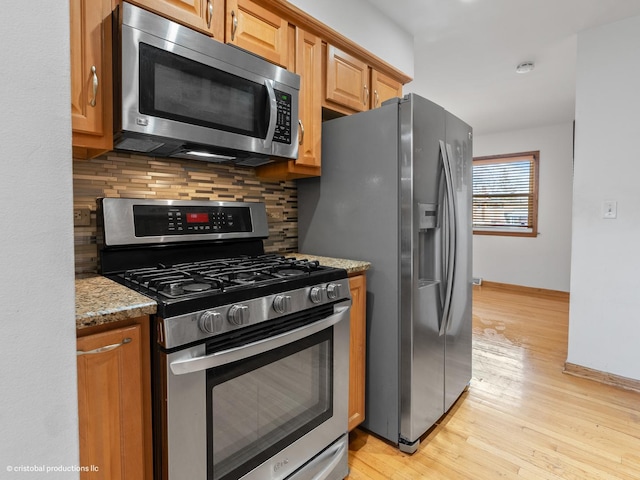 kitchen with tasteful backsplash, baseboards, light stone countertops, light wood-style flooring, and stainless steel appliances