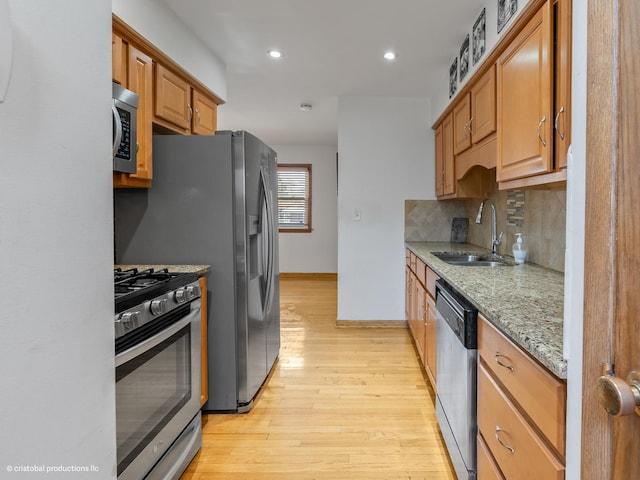 kitchen featuring backsplash, light wood-type flooring, light stone counters, appliances with stainless steel finishes, and a sink