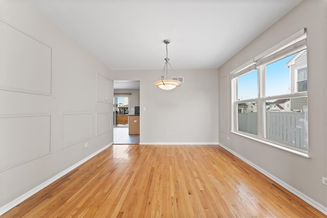 unfurnished dining area with light wood-type flooring, baseboards, and a decorative wall