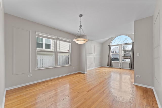 empty room featuring light wood-style floors, vaulted ceiling, and baseboards