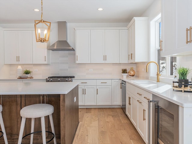 kitchen featuring wall chimney exhaust hood, dishwasher, sink, white cabinetry, and wine cooler