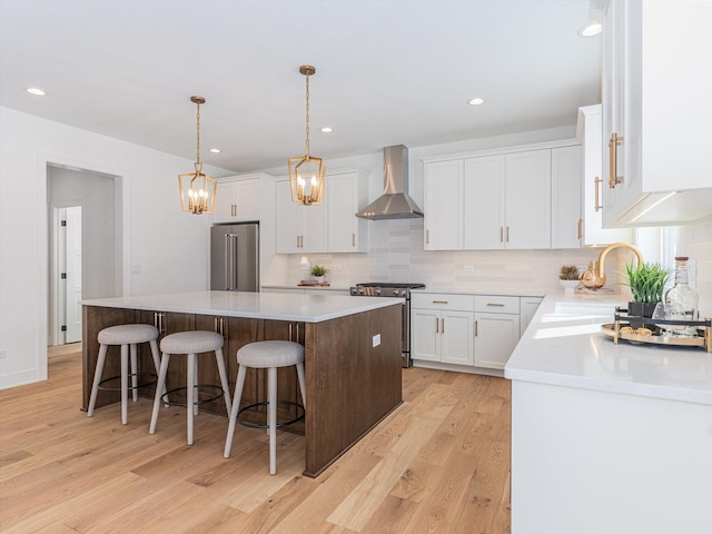 kitchen featuring a center island, white cabinetry, light hardwood / wood-style floors, stainless steel appliances, and wall chimney exhaust hood