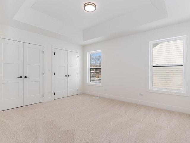 unfurnished bedroom with a raised ceiling, multiple closets, and light colored carpet