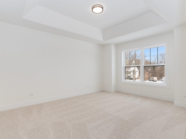 empty room with a raised ceiling and light colored carpet