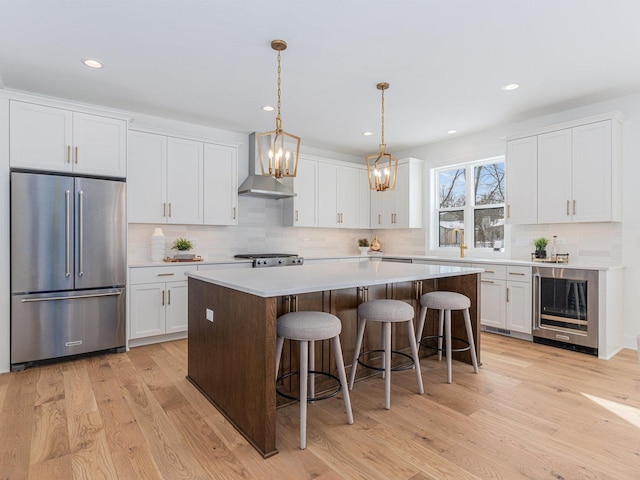 kitchen with white cabinetry, a center island, high end refrigerator, wine cooler, and wall chimney range hood