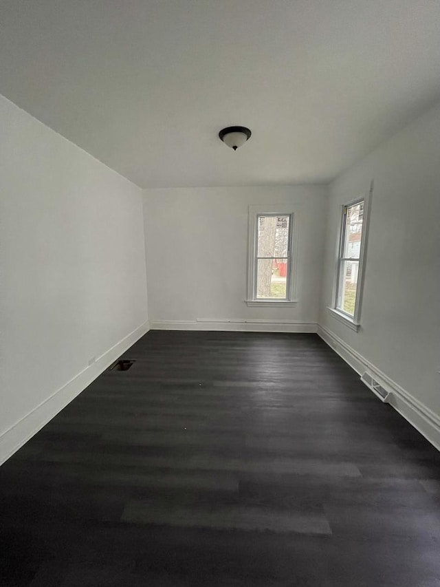 spare room featuring dark wood-type flooring, visible vents, and baseboards