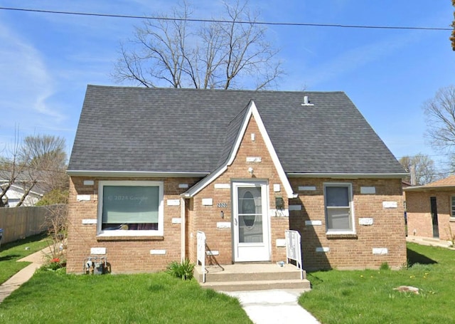 tudor house with brick siding, a shingled roof, fence, and a front yard