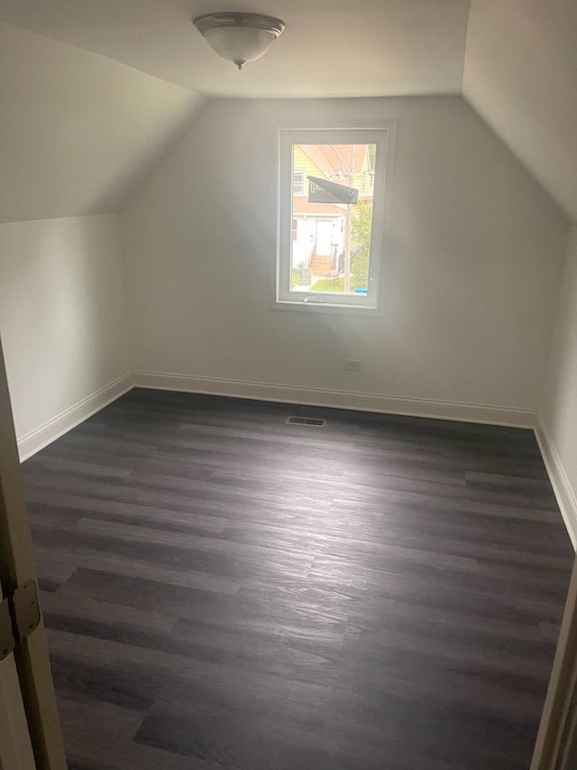 additional living space featuring lofted ceiling, dark wood-style floors, baseboards, and visible vents