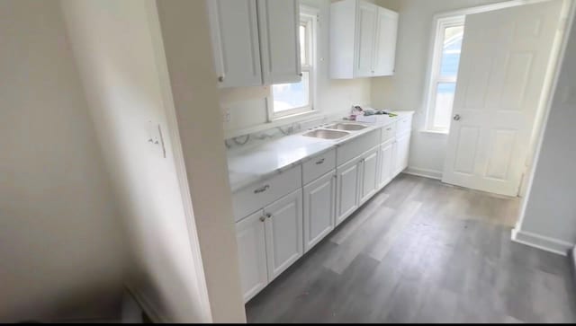 kitchen featuring light countertops, light wood-style floors, white cabinetry, a sink, and baseboards