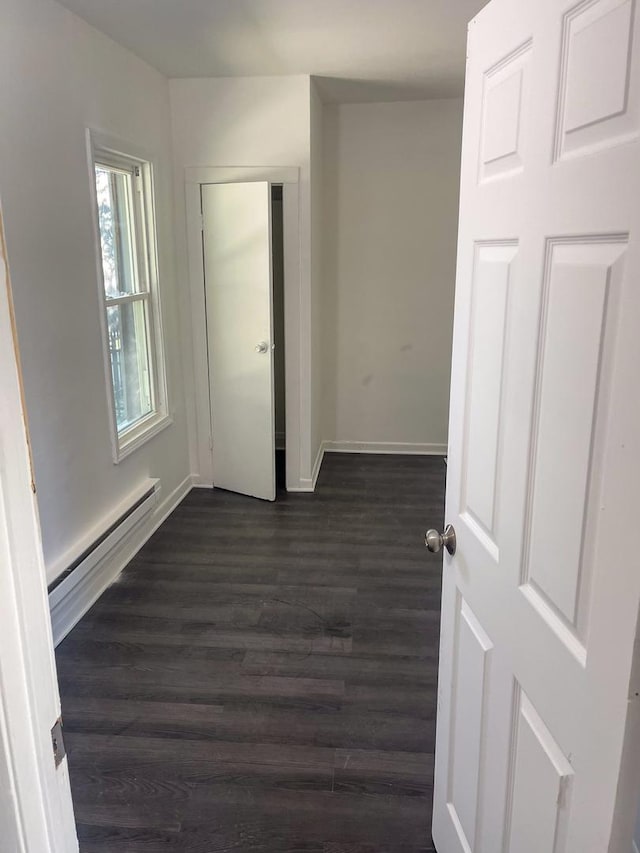 spare room featuring a baseboard radiator, baseboards, and dark wood-style flooring