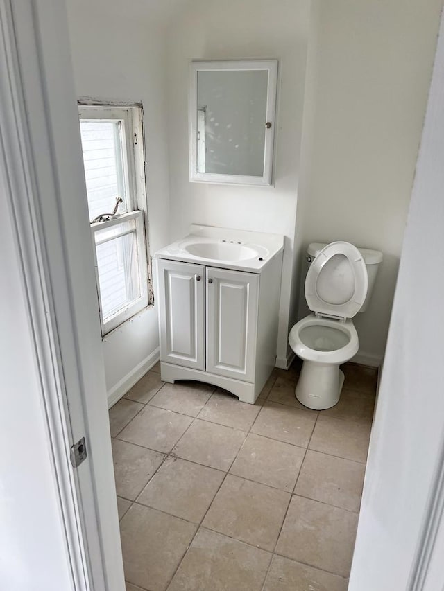 half bath with baseboards, toilet, vanity, and tile patterned floors