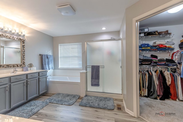 full bathroom featuring a garden tub, wood finished floors, vanity, a spacious closet, and a shower stall