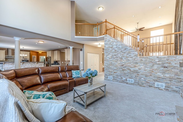 living area featuring carpet floors, visible vents, ornate columns, and ceiling fan with notable chandelier