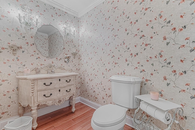 half bath featuring toilet, crown molding, wood finished floors, vanity, and wallpapered walls