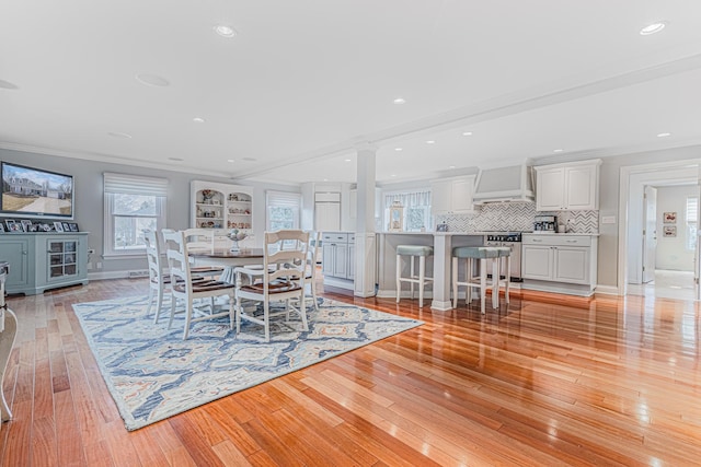 unfurnished dining area featuring recessed lighting, crown molding, baseboards, light wood finished floors, and ornate columns