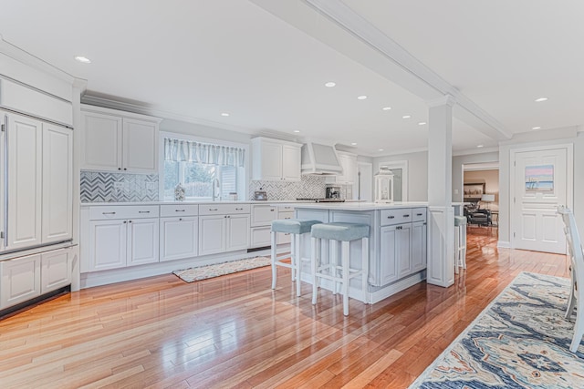 kitchen with light countertops, a center island, white cabinetry, a breakfast bar, and custom exhaust hood