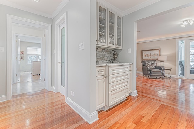 corridor featuring baseboards, ornamental molding, and light wood-style floors