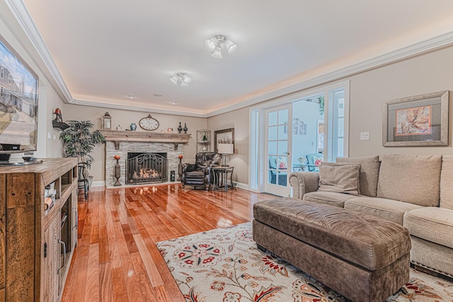 living area featuring a lit fireplace, ornamental molding, wood finished floors, and baseboards