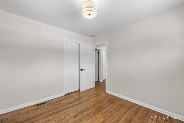 spare room with wood finished floors, visible vents, and baseboards