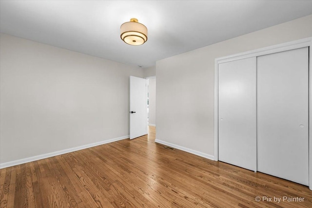 unfurnished bedroom with a closet, wood finished floors, visible vents, and baseboards