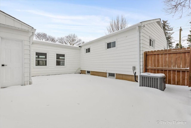 snow covered rear of property featuring fence and central AC unit