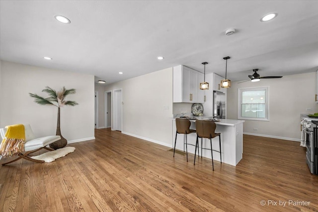 kitchen featuring white cabinets, light wood-style flooring, appliances with stainless steel finishes, decorative light fixtures, and a peninsula