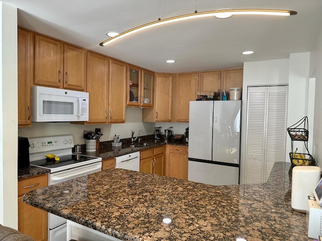 kitchen with a sink, white appliances, dark stone counters, recessed lighting, and glass insert cabinets