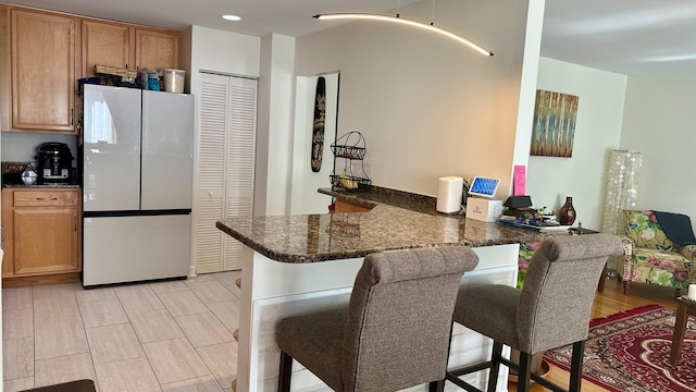 kitchen with freestanding refrigerator, a peninsula, a kitchen breakfast bar, recessed lighting, and dark stone countertops