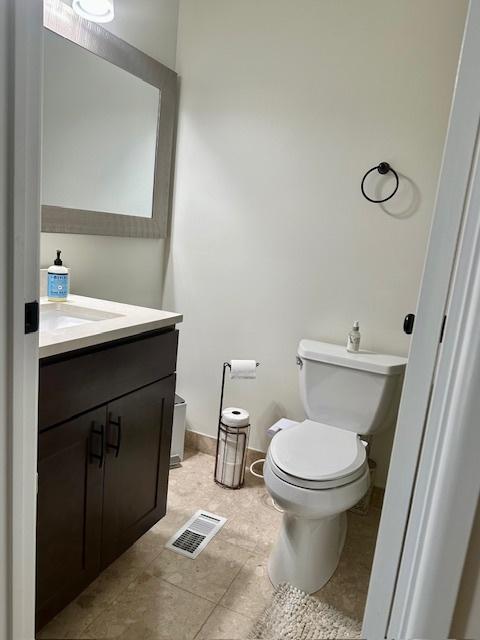 half bathroom featuring vanity, tile patterned flooring, toilet, and visible vents