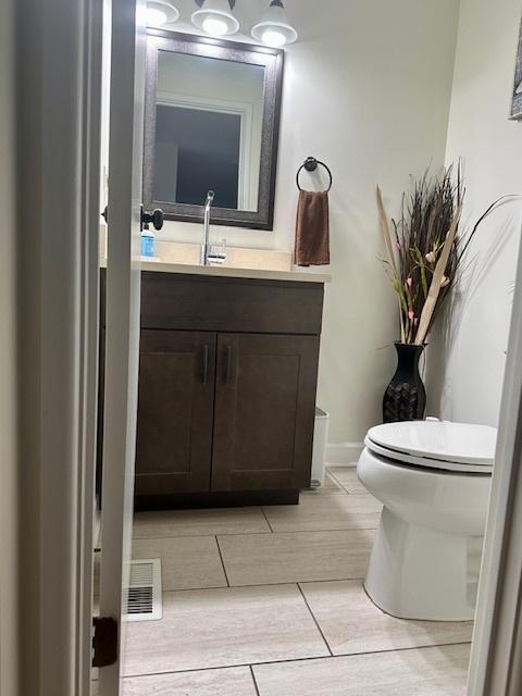 half bath with toilet, wood tiled floor, and vanity
