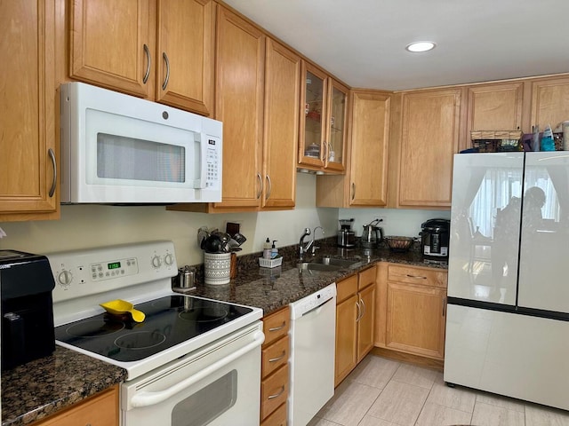 kitchen with white appliances, glass insert cabinets, a sink, and dark stone countertops