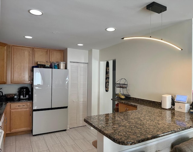 kitchen featuring recessed lighting, freestanding refrigerator, dark stone countertops, and a peninsula