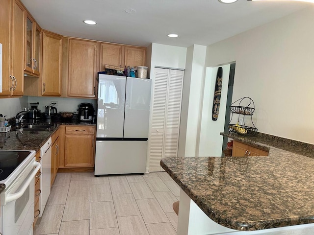 kitchen with a sink, white appliances, dark stone counters, recessed lighting, and glass insert cabinets