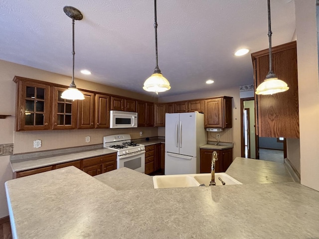 kitchen featuring white appliances, a sink, light countertops, hanging light fixtures, and glass insert cabinets