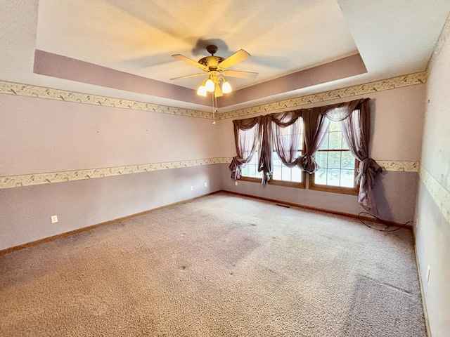 spare room with ceiling fan, carpet floors, visible vents, baseboards, and a raised ceiling