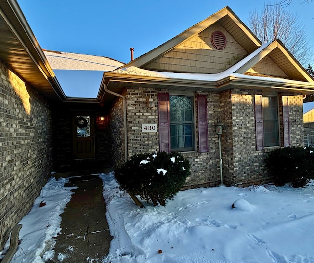 snow covered property entrance featuring brick siding