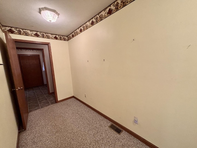 unfurnished room with carpet, visible vents, a textured ceiling, and baseboards