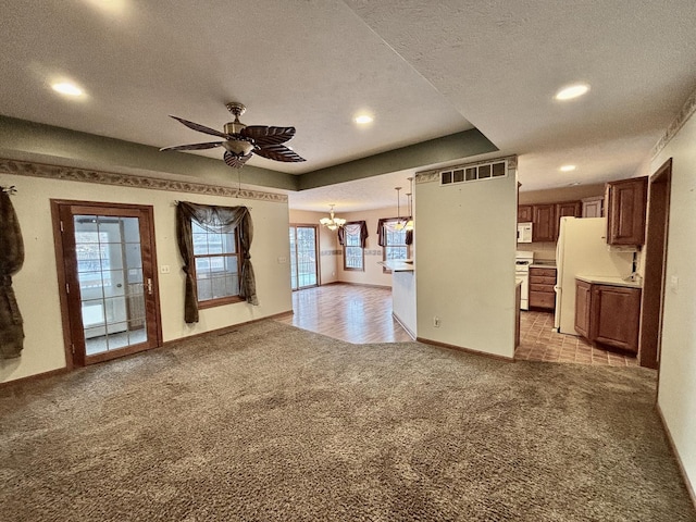 unfurnished living room with ceiling fan with notable chandelier, a raised ceiling, visible vents, and light colored carpet